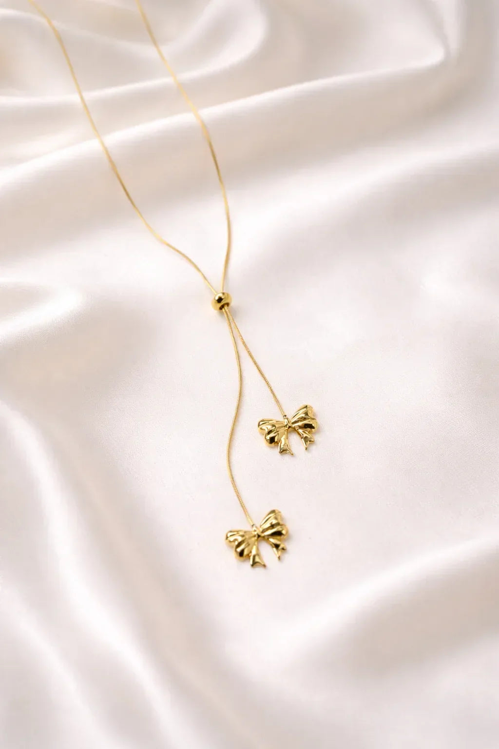 Gold butterfly pendant necklace with delicate chain on white satin fabric