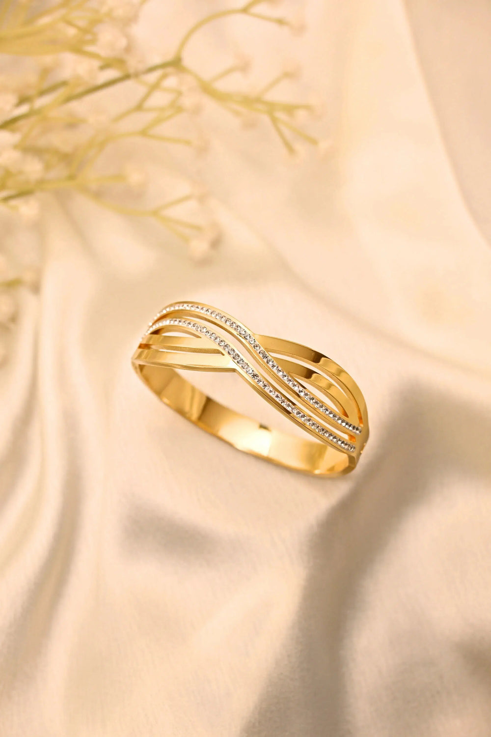 Elegant gold bracelet with wavy design and embedded stones on soft beige fabric