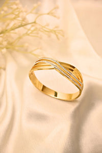 gold bangle with crisscross design and small embedded stones on cream fabric background