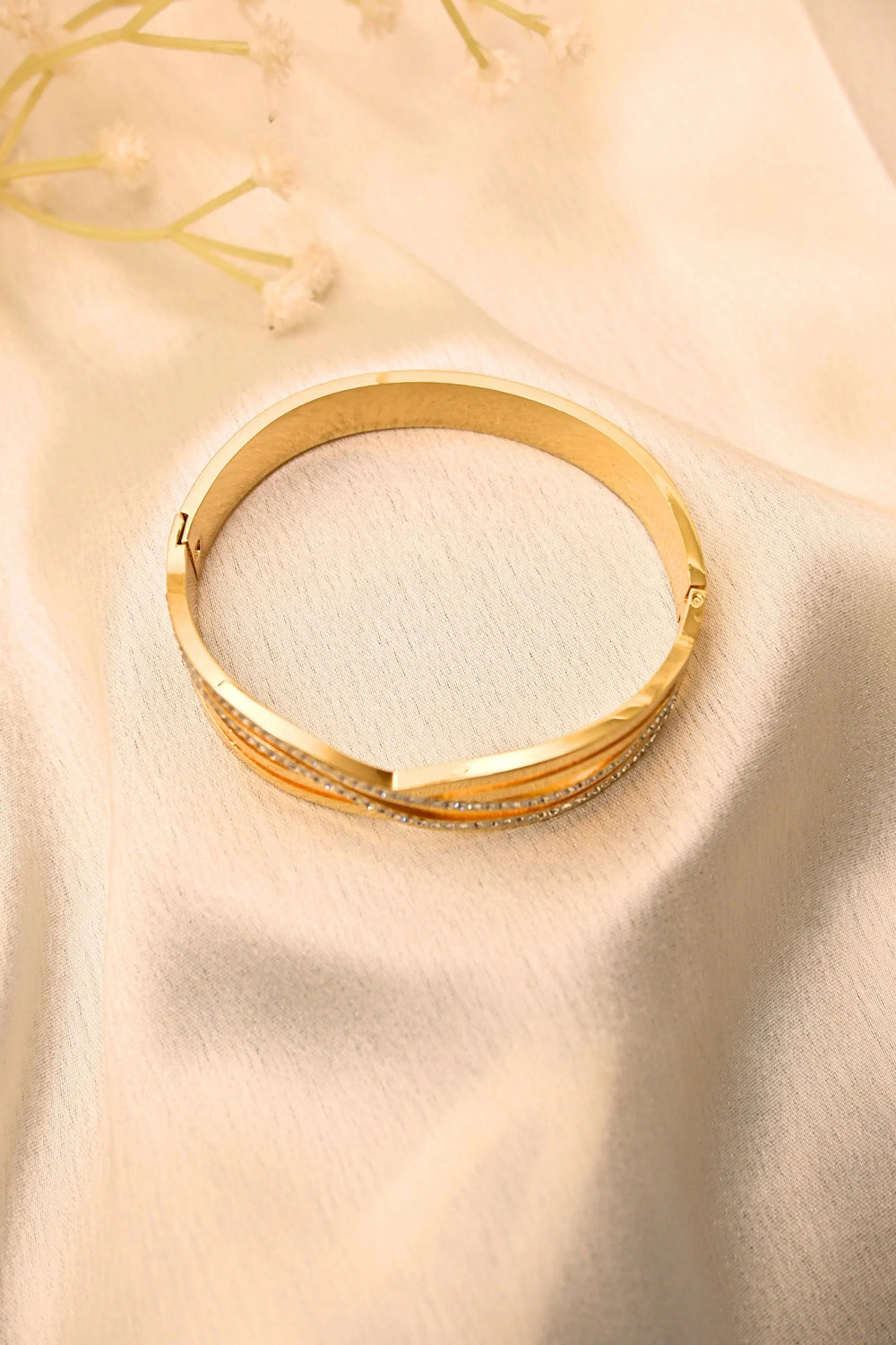 Gold bangle bracelet with textured accents and embedded stones on soft cream fabric