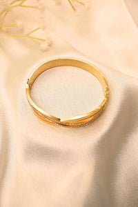 Gold bangle bracelet with textured accents and embedded stones on soft cream fabric