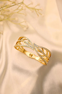 Gold designer bracelet with leaf motif and embedded stones on a cream fabric background