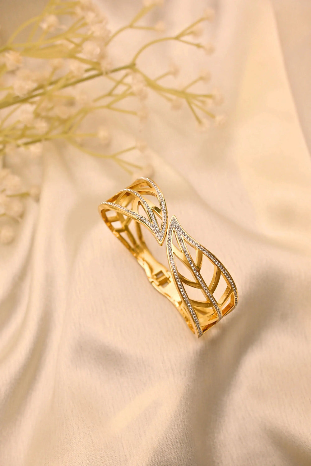 Gold openwork bangle bracelet with leaf pattern and small sparkling stones on cream fabric