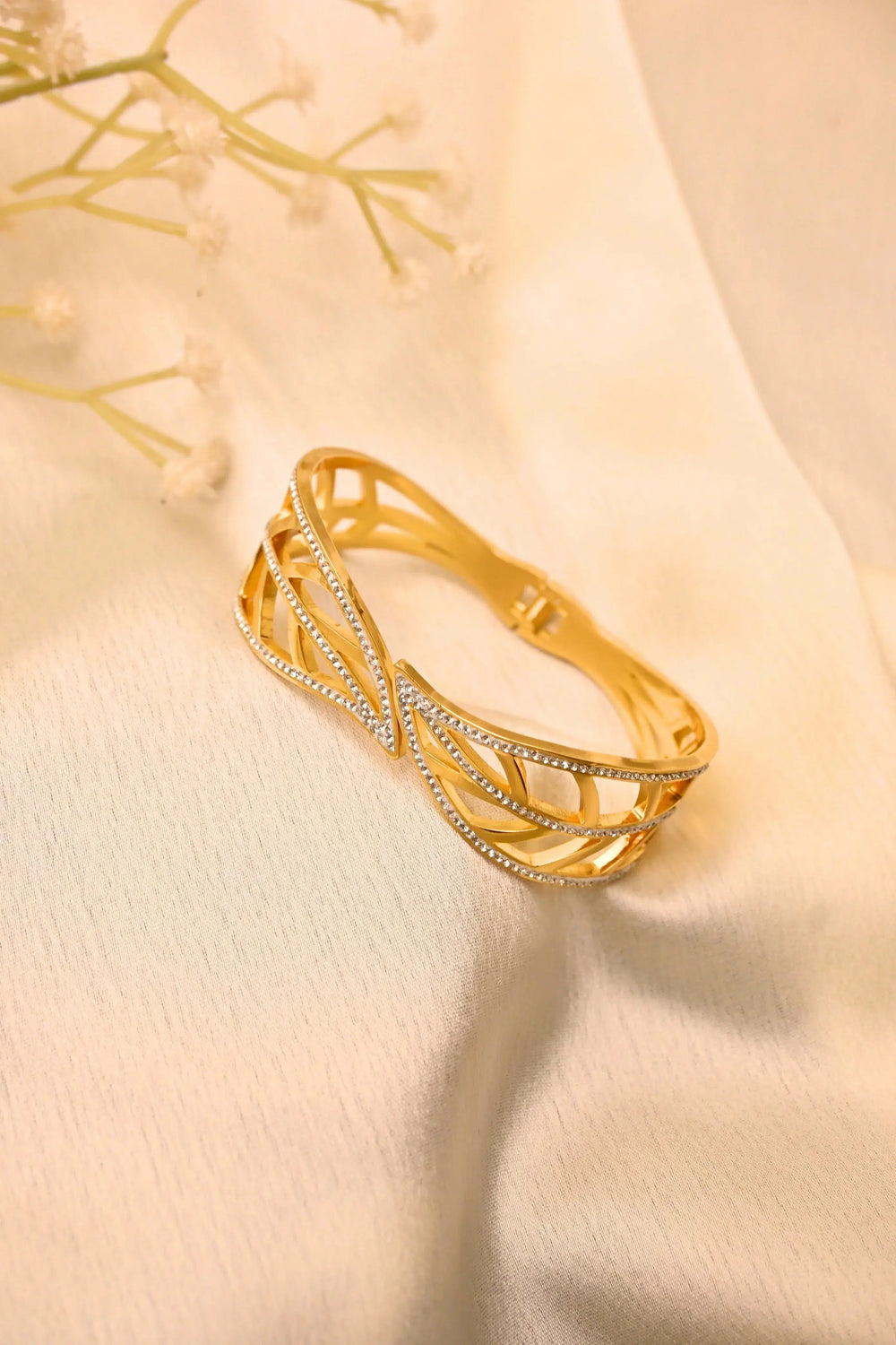 Gold bangle bracelet with intricate openwork and crystal accents on a cream fabric background