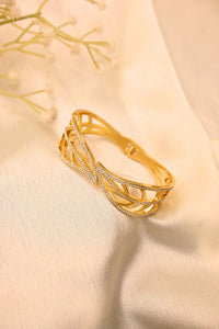 Gold bangle bracelet with intricate openwork and crystal accents on a cream fabric background