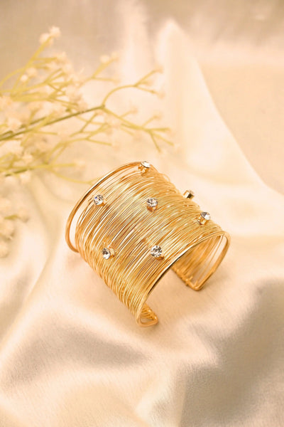 Gold wire cuff bracelet with sparkling crystal accents on a beige fabric background