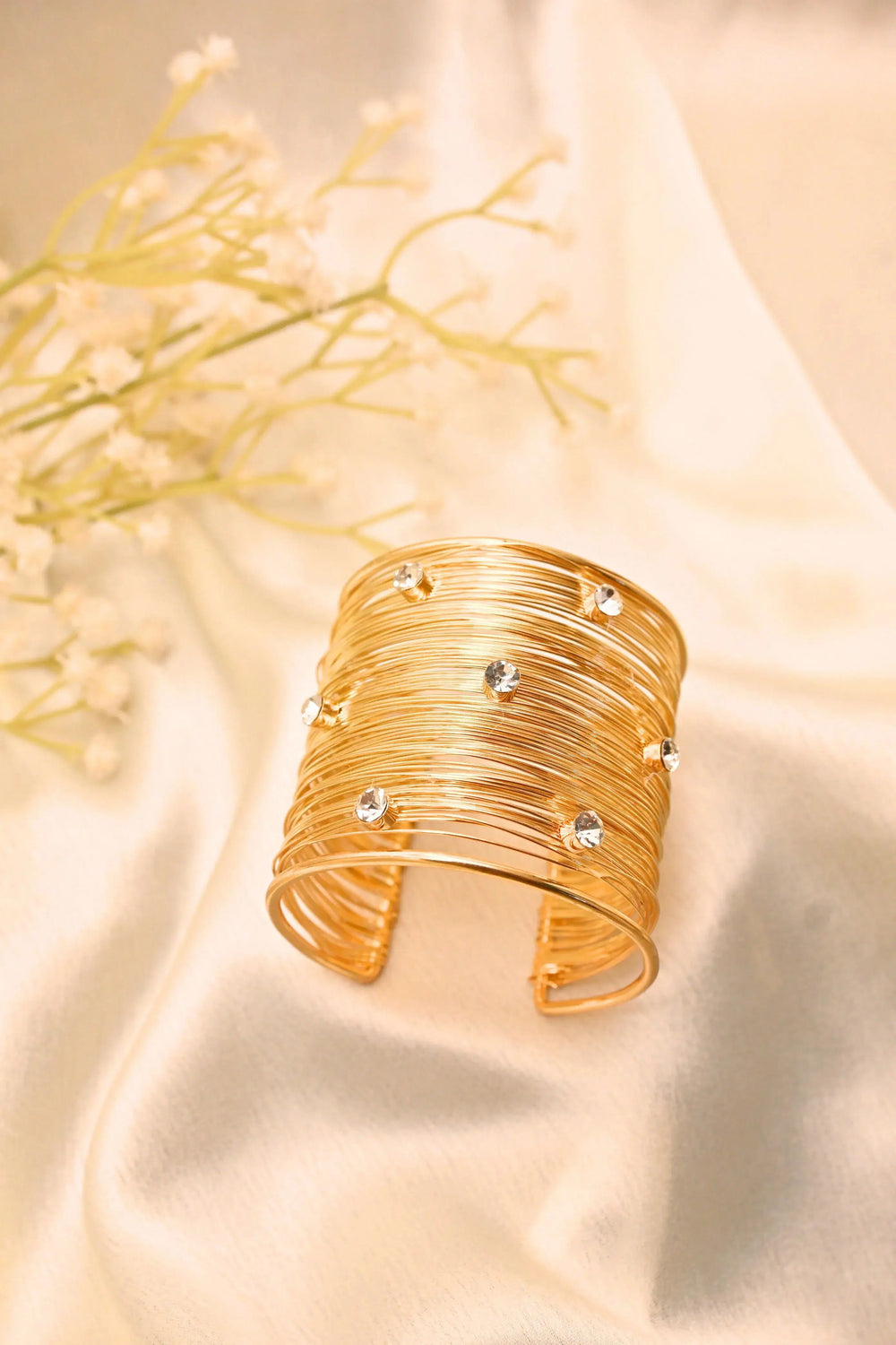 Gold wire cuff bracelet with clear stones on satin fabric background
