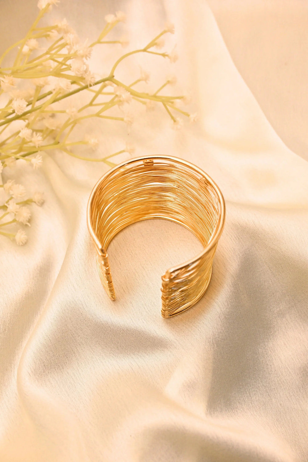 Textured gold cuff bracelet on cream fabric with delicate floral accents