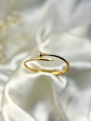 Gold nail-shaped diamond bangle bracelet on white fabric background