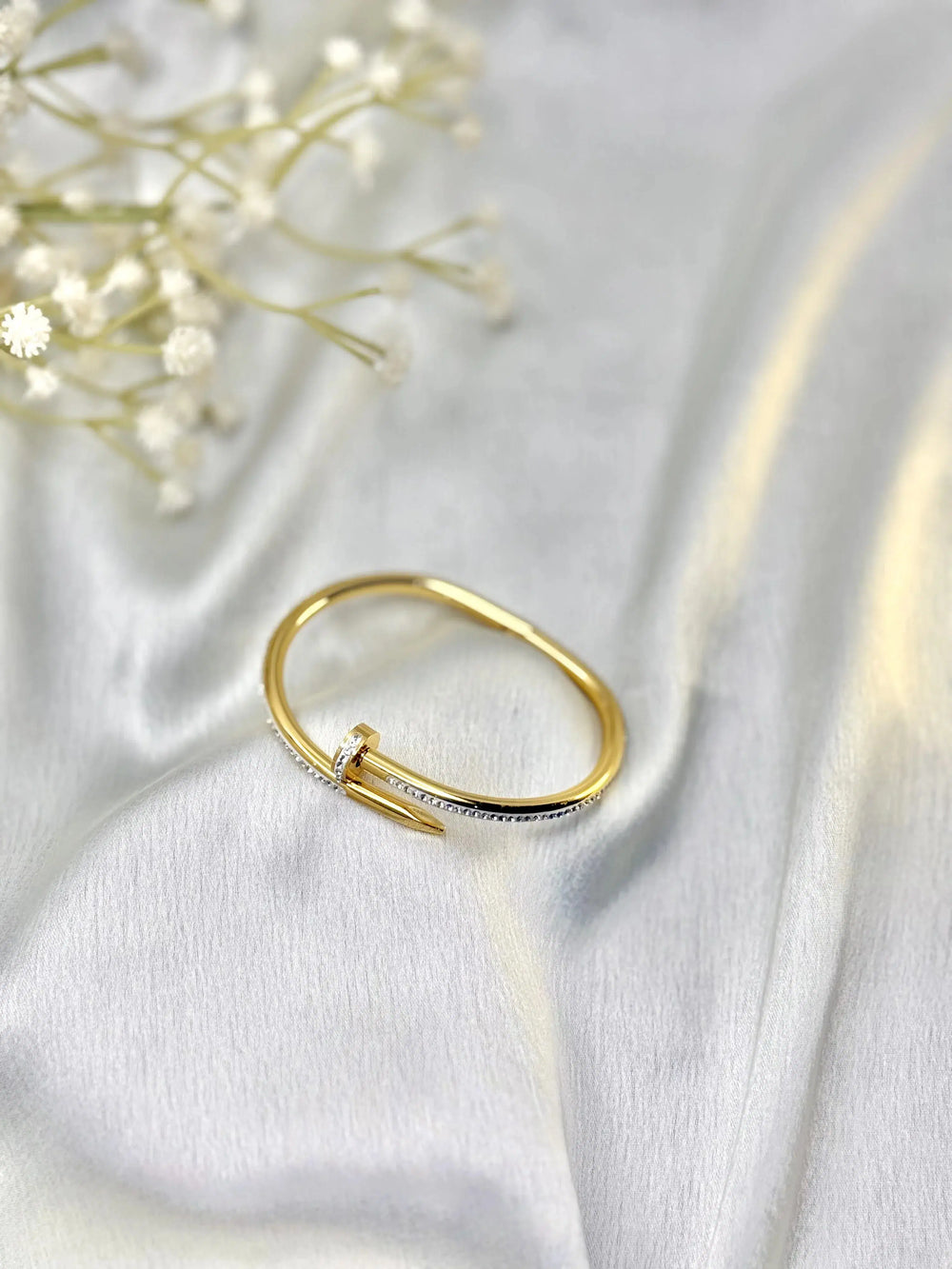 Gold nail-shaped diamond ring on white satin fabric with delicate white flowers
