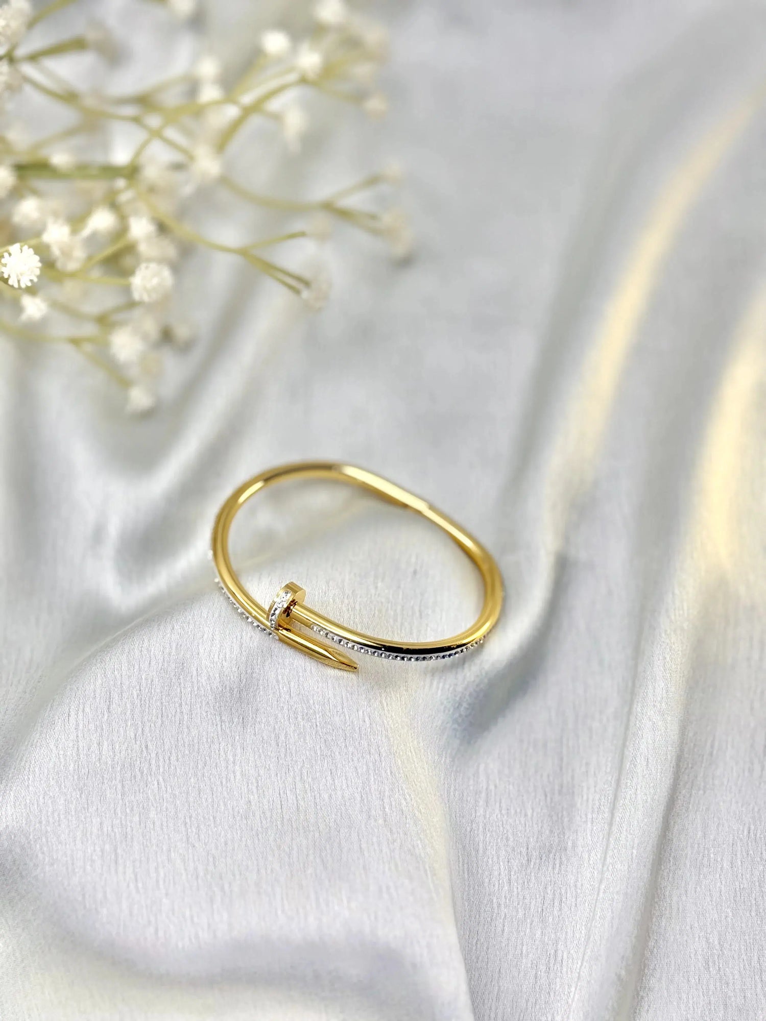 Gold nail-shaped diamond ring on white satin fabric with delicate white flowers