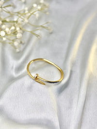 Gold nail-shaped diamond ring on white satin fabric with delicate white flowers
