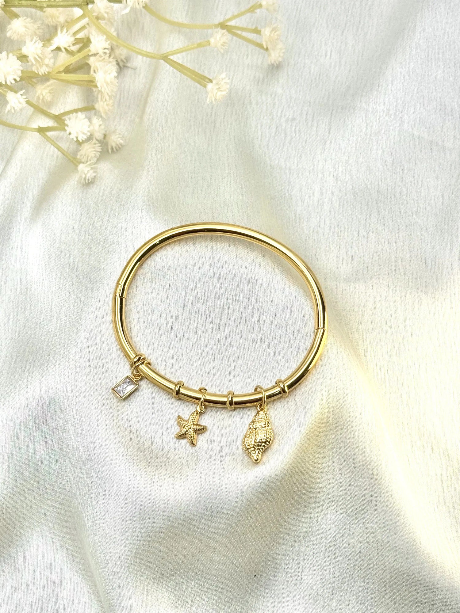 Gold charm bracelet with starfish, shell, and crystal charms on silk fabric