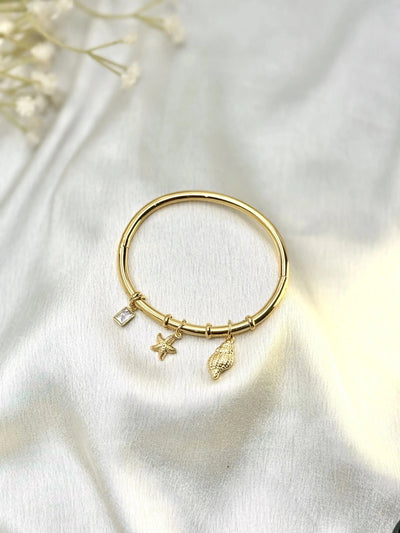 Gold charm bracelet with starfish, shell, and crystal pendant on white satin fabric
