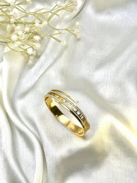 Gold geometric designer bangle with white stones on soft white fabric, elegant jewelry