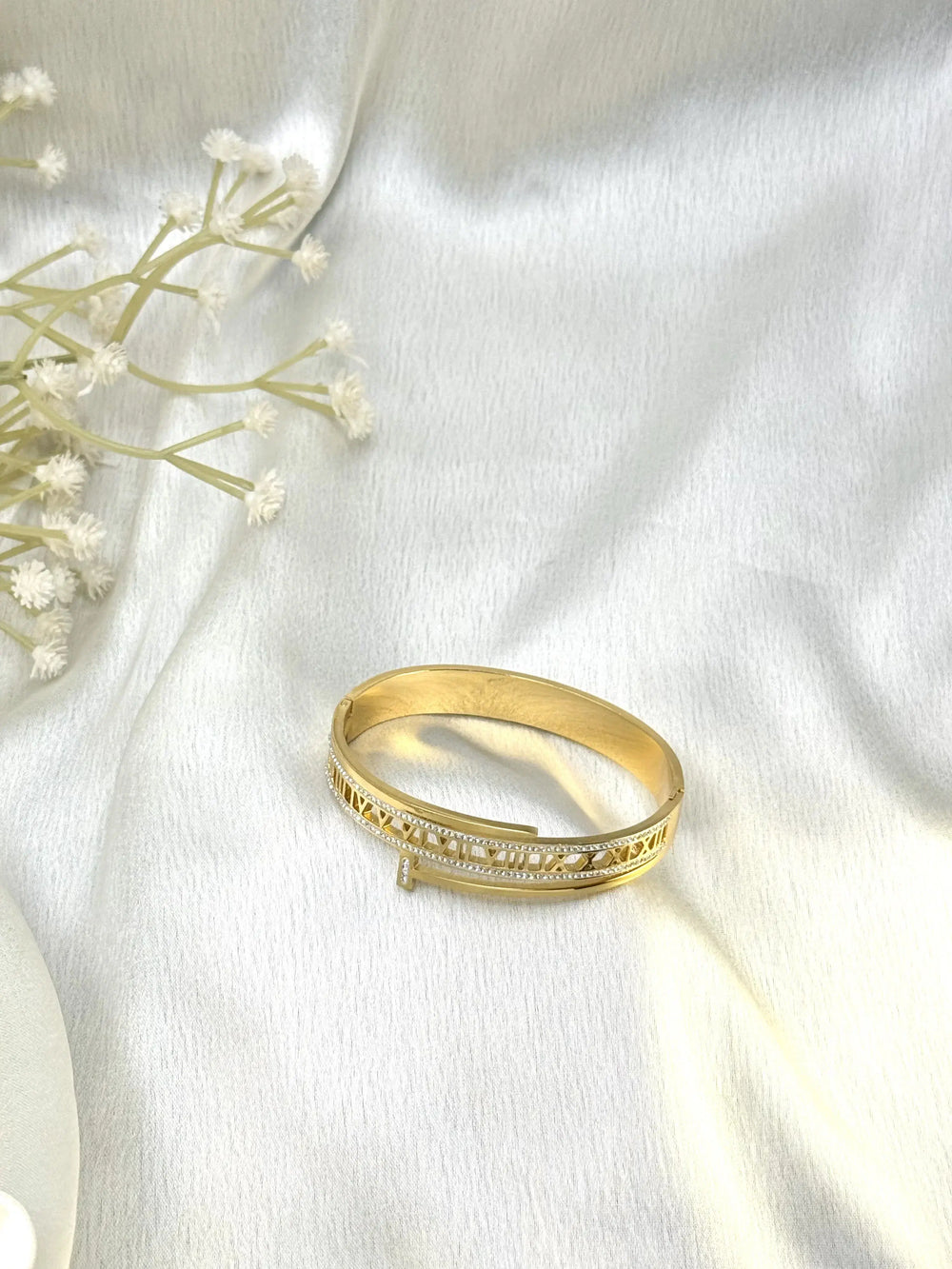 Elegant gold bangle bracelet with diamond accents on white satin fabric background