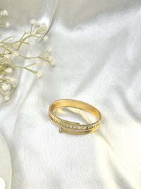 Elegant gold bangle bracelet with diamond accents on white satin fabric background