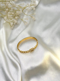 Gold bracelet with rectangular diamond centerpiece on white satin fabric, floral accent