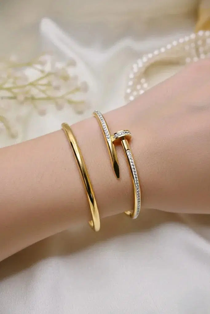 Gold bangle and diamond-studded nail-shaped bracelet on wrist with soft background
