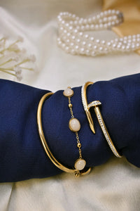 Elegant gold bracelets with white stones and crystal accents on blue fabric, pearl necklace in background