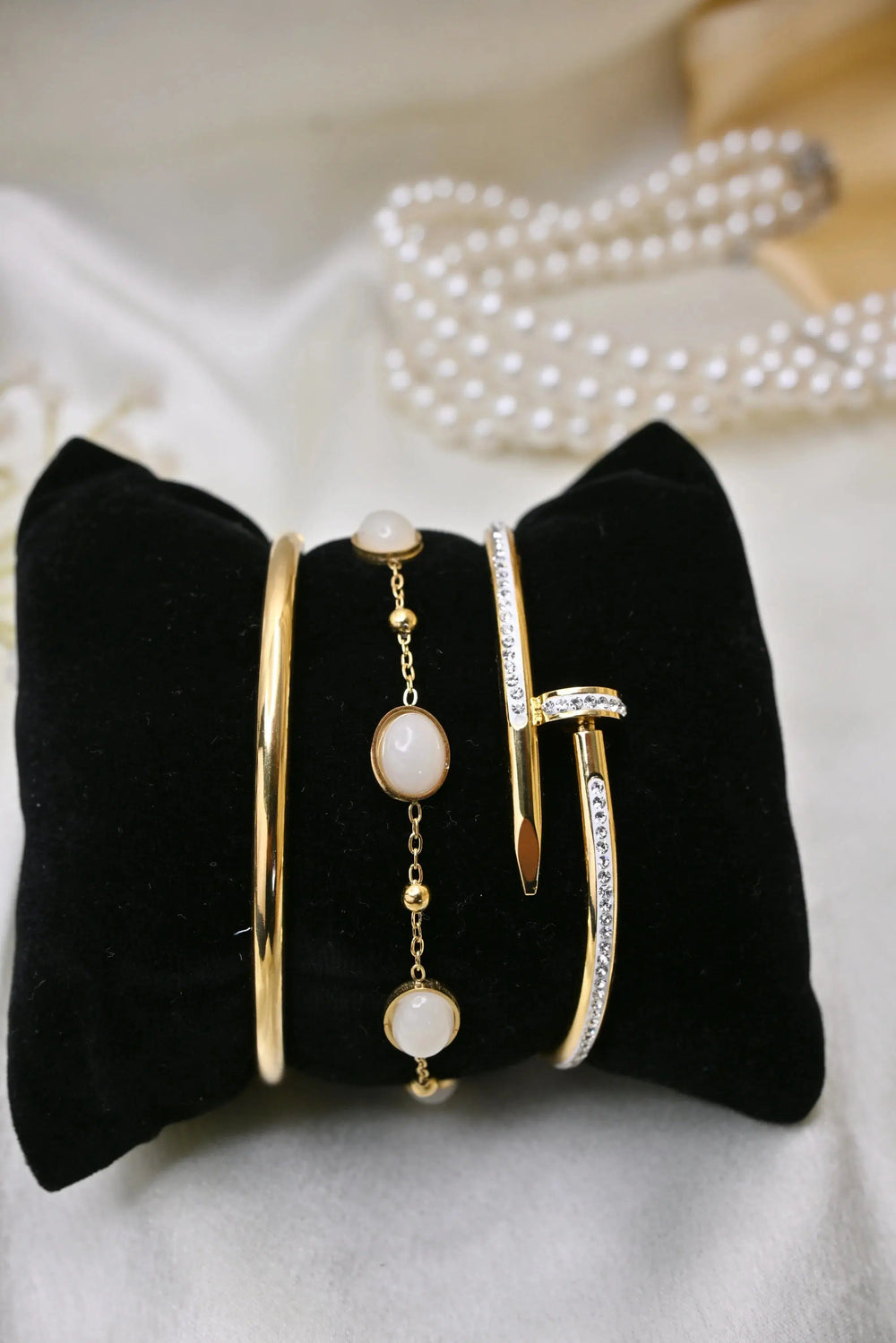 Gold and crystal bangle bracelets with pearls on a black velvet display pillow