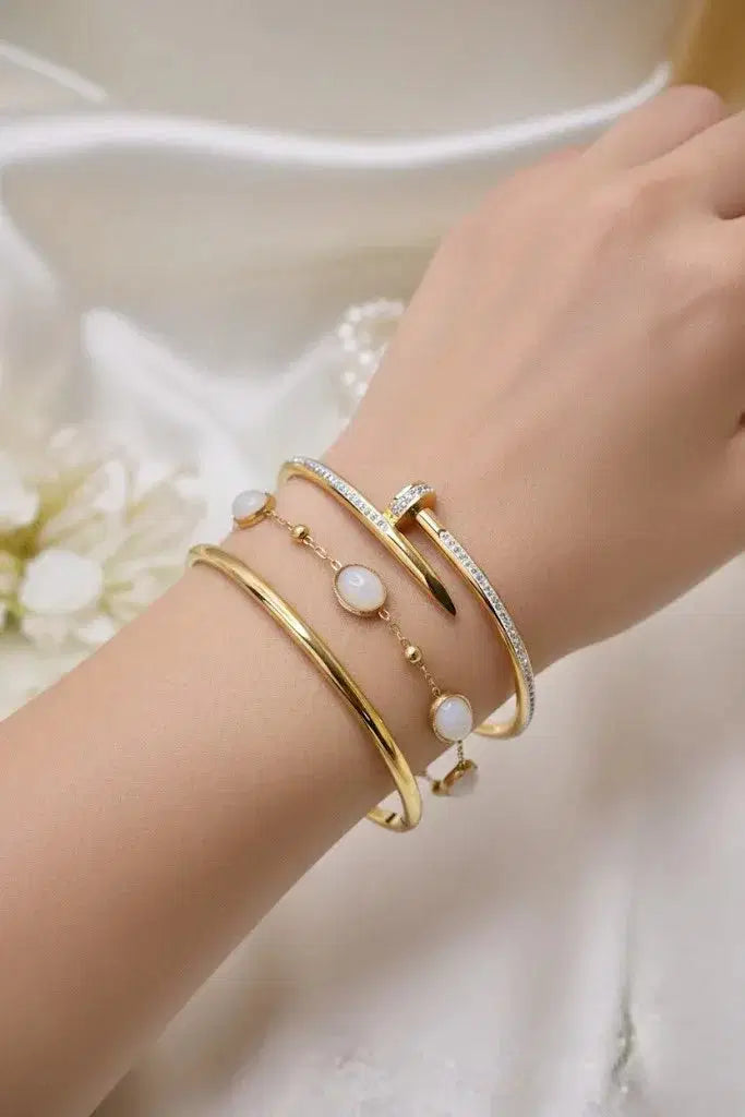 Woman’s wrist adorned with stacked gold bangles and white stone bracelet on satin background