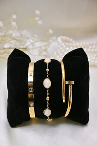 Three elegant gold bracelets displayed on a black velvet cushion with pearls in background