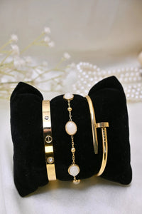 Elegant gold bracelets with white stones and crystal accents displayed on a black cushion.