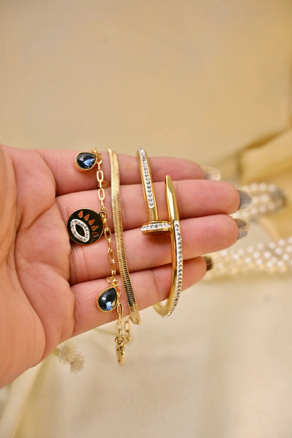 Hand holding assorted gold bracelets and bangles with gemstones and crystal details
