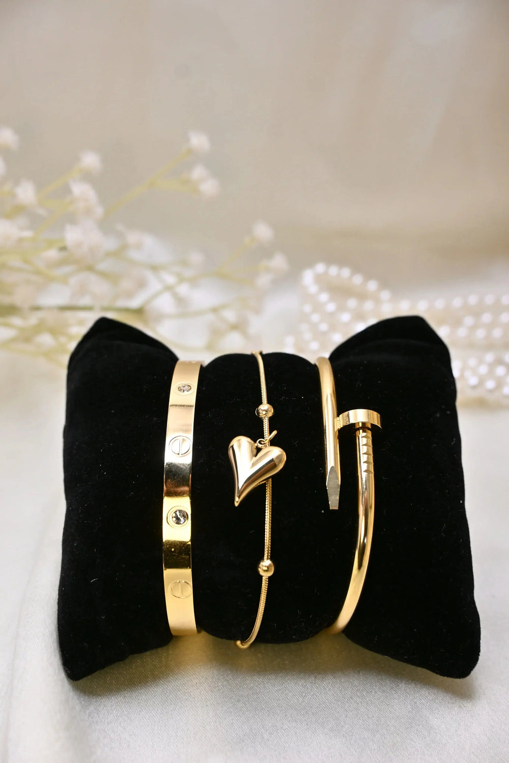 Gold bracelets with heart charm and screw motifs displayed on a black velvet cushion