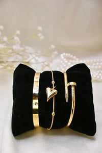 Gold bracelets with heart charm and screw motifs displayed on a black velvet cushion