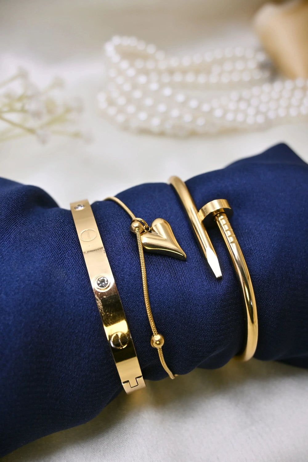 Elegant gold bracelets and heart-shaped pendant on navy fabric, pearl necklace in background