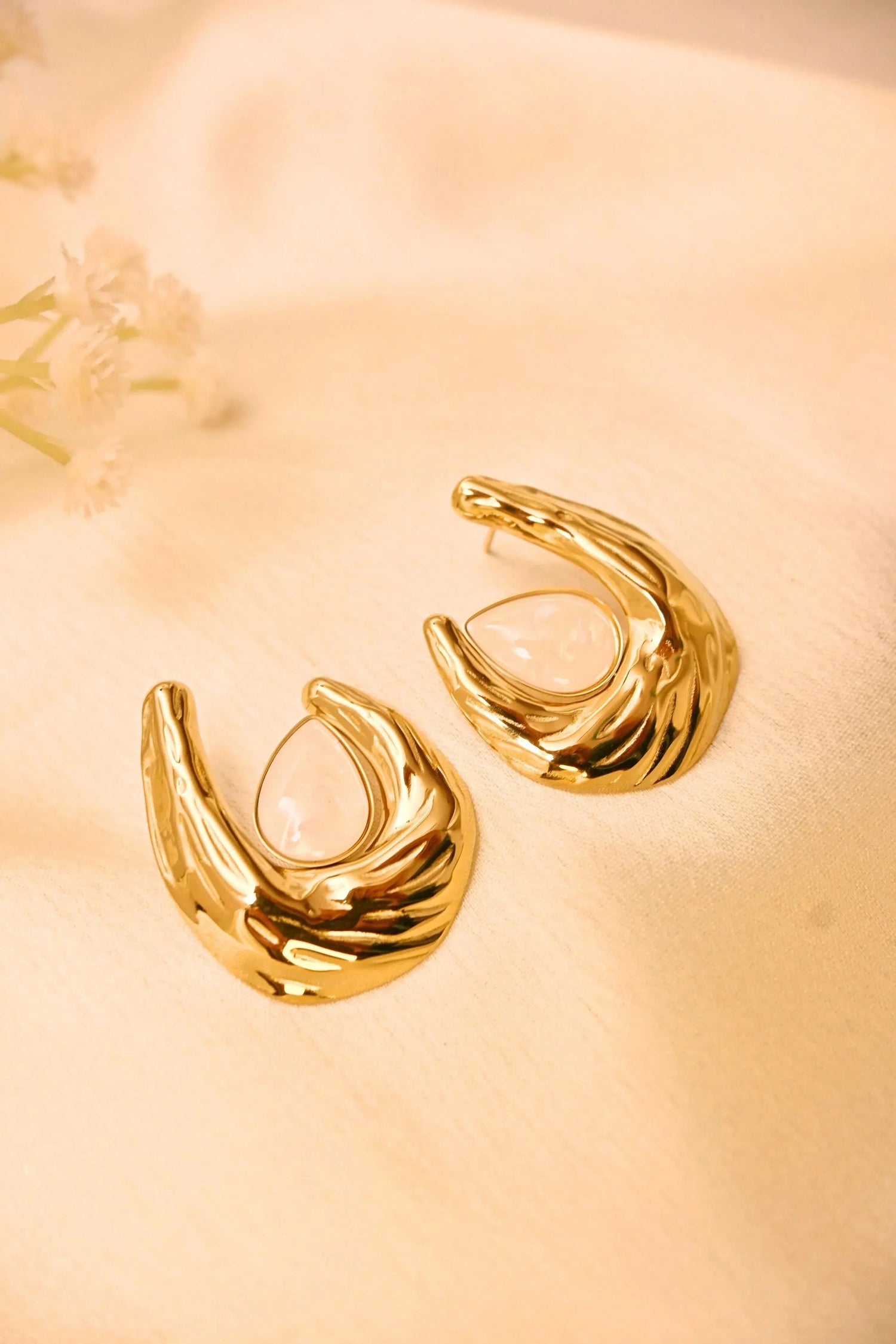 Gold statement earrings with textured finish and teardrop gemstone on soft fabric