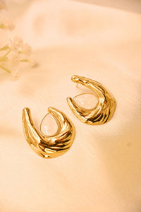 Gold statement earrings with textured finish and teardrop gemstone on soft fabric