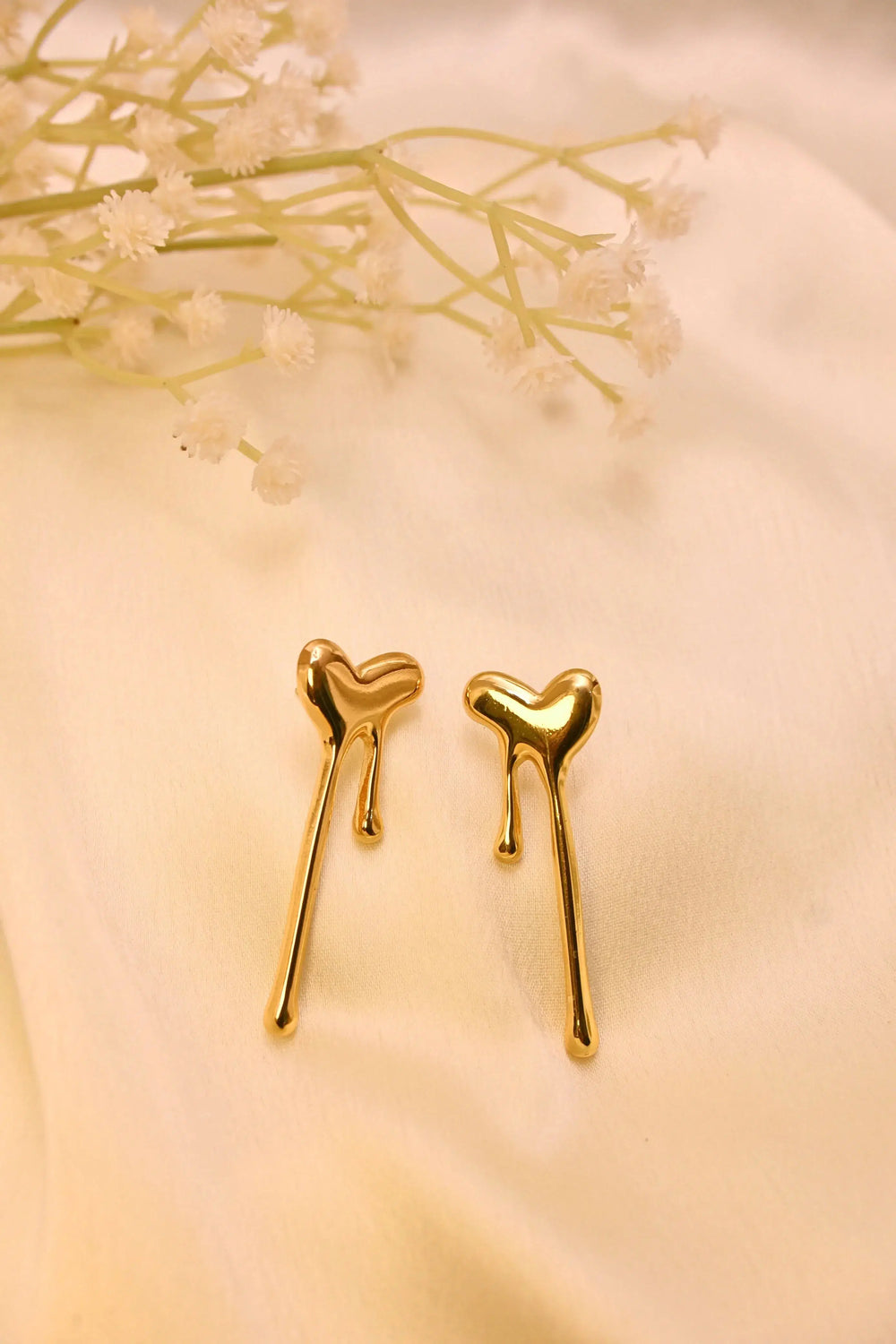Gold heart drop earrings with a modern, melted design on a soft cream fabric background