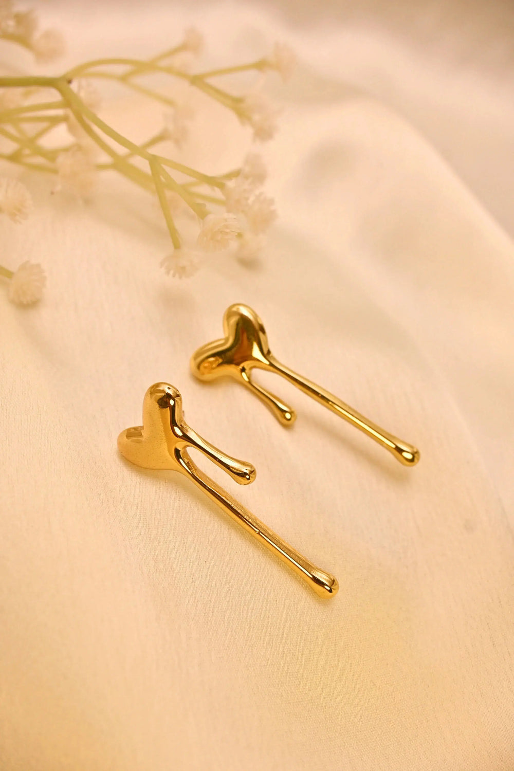 Gold heart-shaped drop earrings on soft beige fabric with delicate white flowers