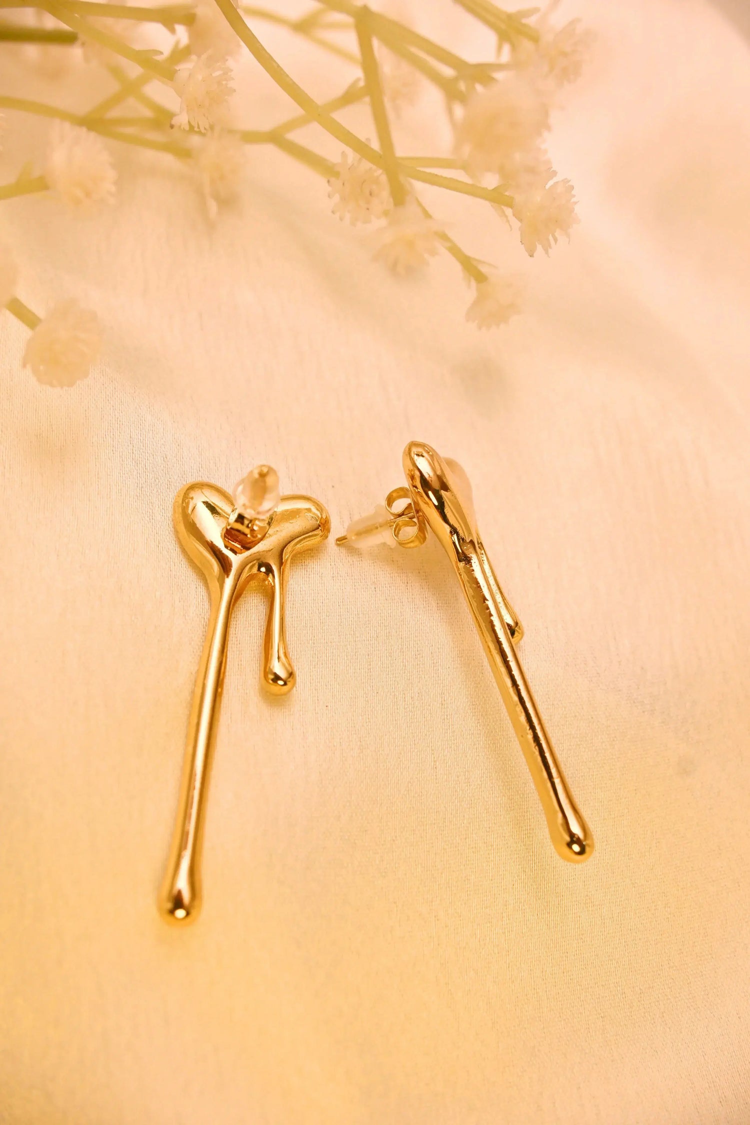 Gold heart-shaped drop earrings with modern design on a cream fabric background