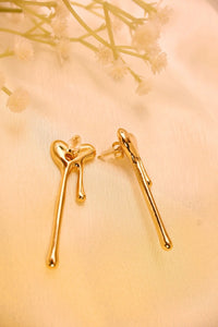 Gold heart-shaped drop earrings with modern design on a cream fabric background