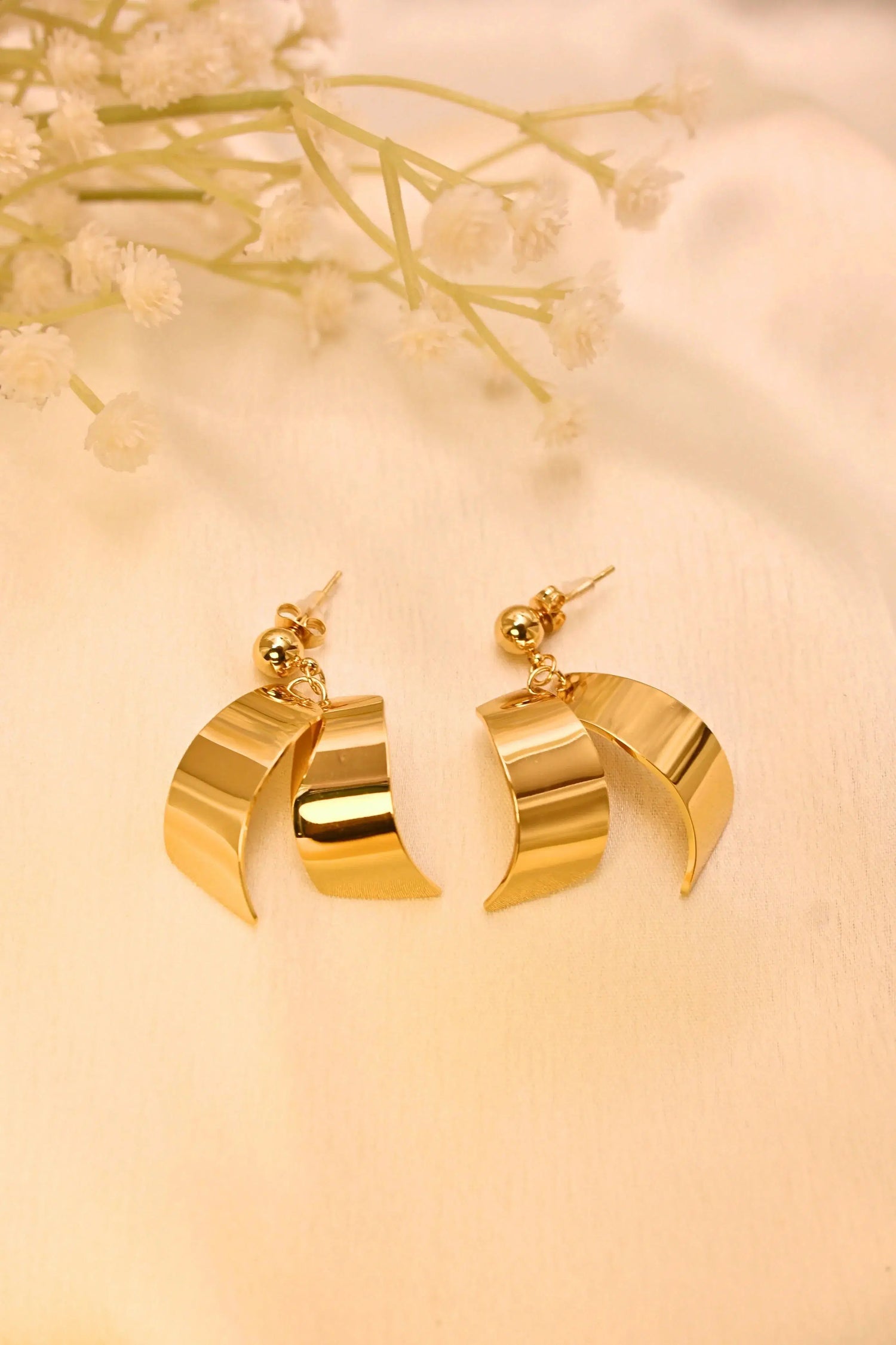 Gold-tone dangle earrings with curved geometric design on cream fabric background