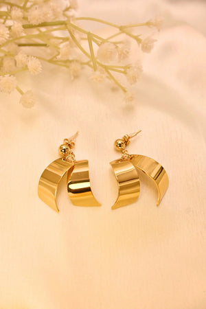 Gold-tone dangle earrings with curved geometric design on cream fabric background