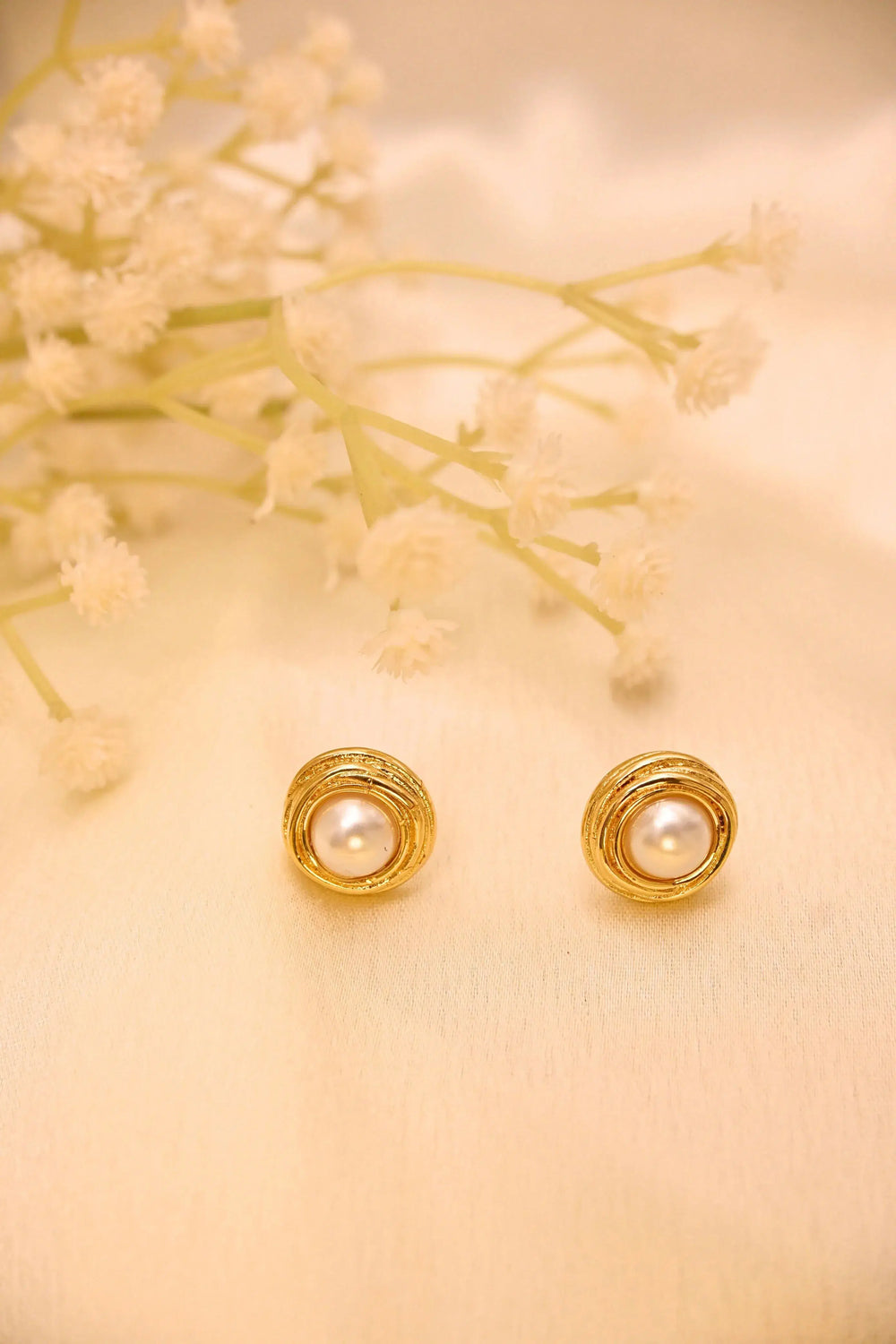Gold round pearl stud earrings on cream fabric with delicate flowers