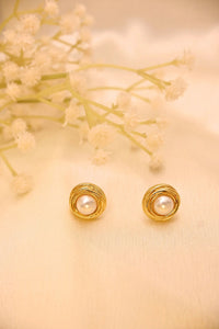 Gold round pearl stud earrings on cream fabric with delicate flowers