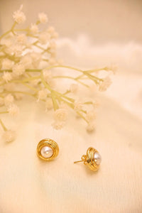 Gold-plated pearl stud earrings on cream fabric with dried white flowers