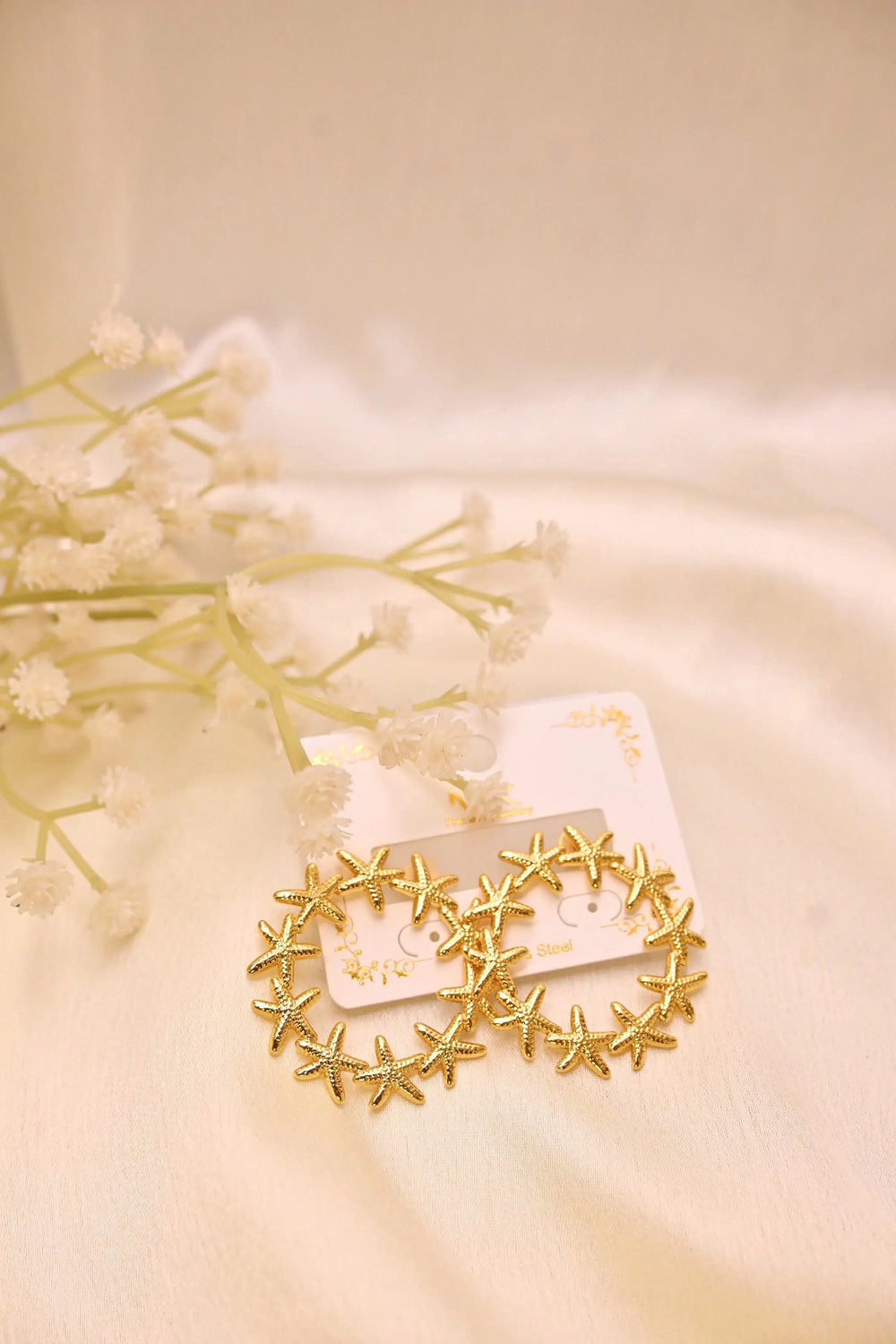 Gold starfish hoop earrings on a soft cream background with delicate white flowers