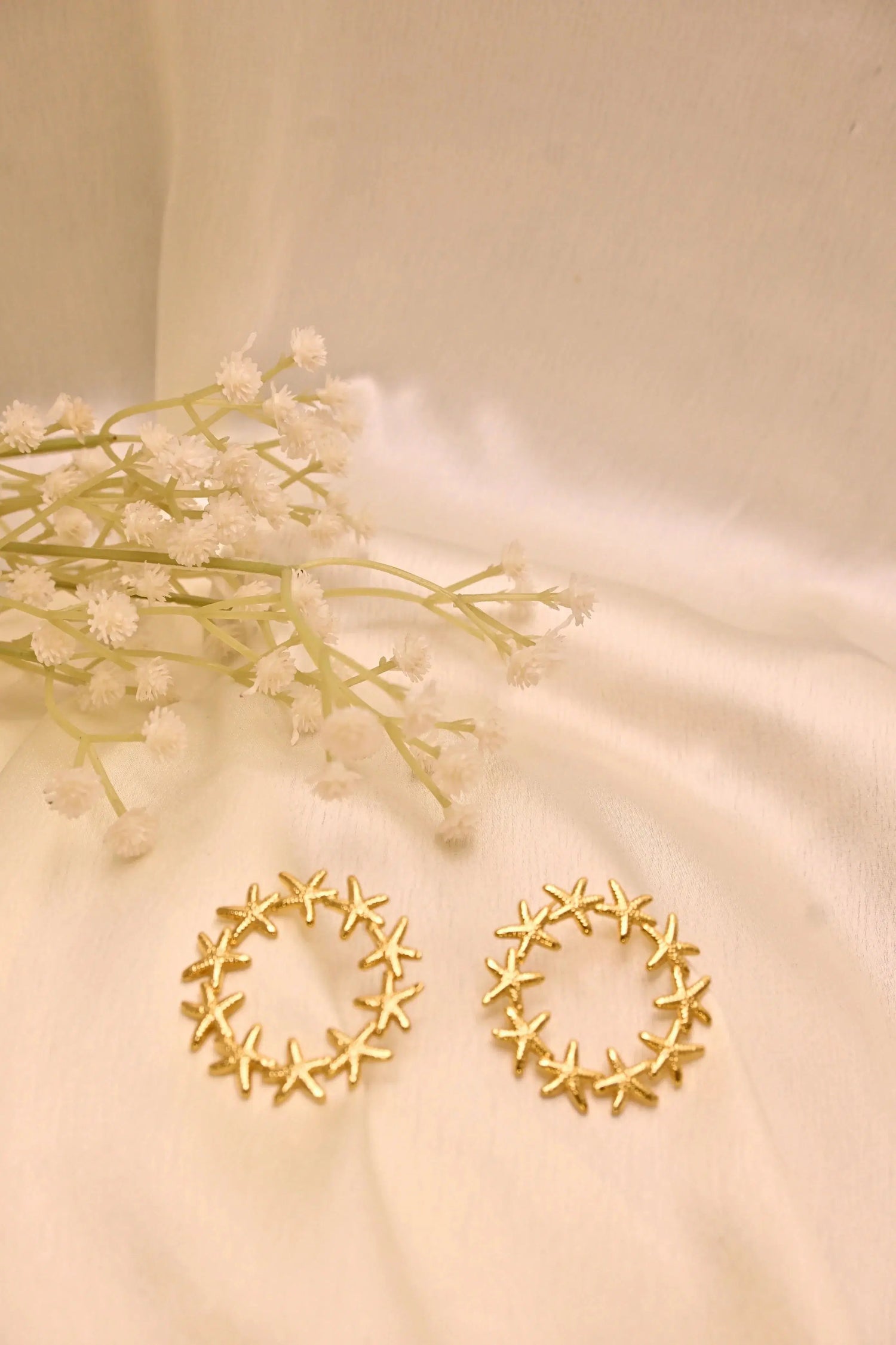 Gold star-shaped hoop earrings on cream fabric with delicate white flowers