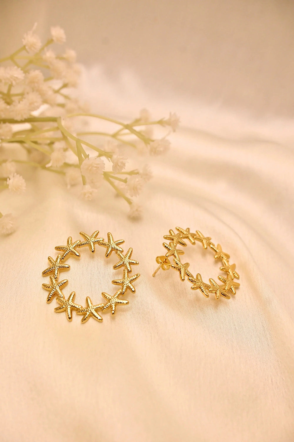 Gold starfish hoop earrings on a cream fabric background with white flowers