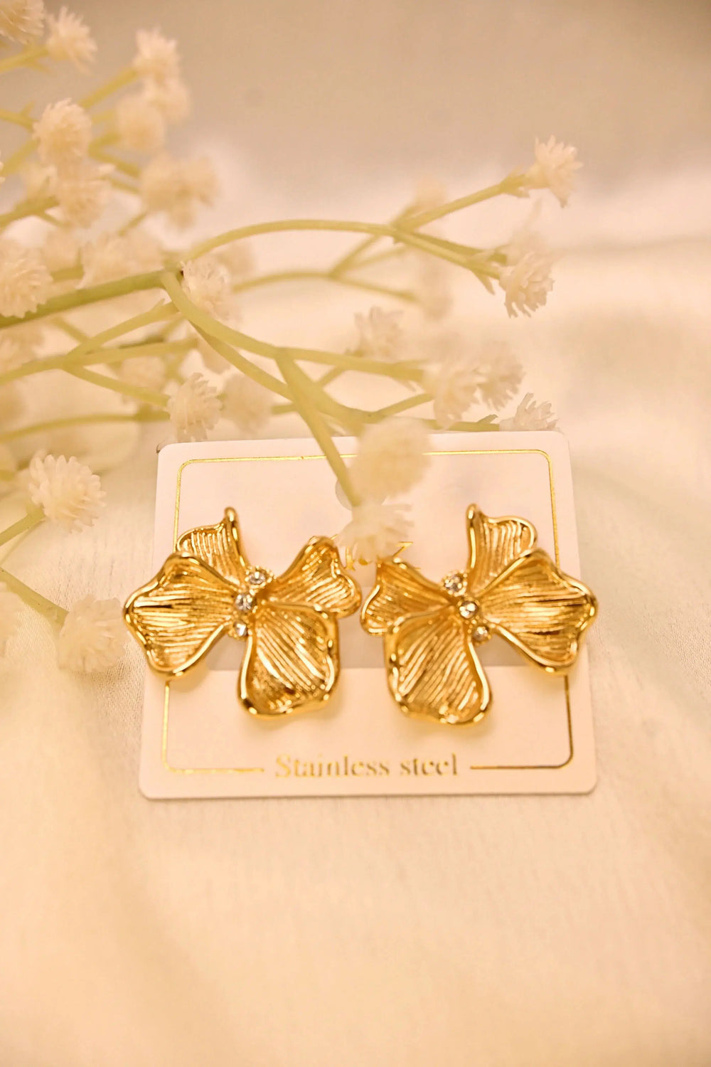 Gold flower-shaped stainless steel earrings with rhinestone centers on a display card