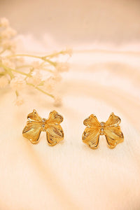 Gold floral stud earrings with textured petals and small gemstones, displayed on a cream fabric
