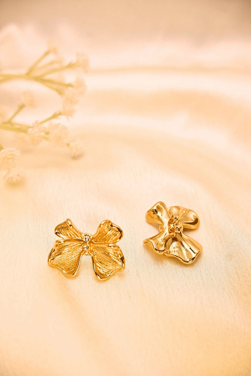 Gold floral stud earrings with textured petals on a soft cream fabric background