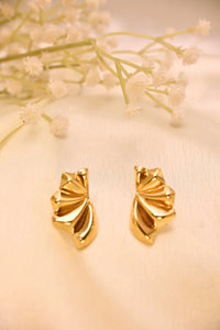 Gold-toned fan-shaped stud earrings on a soft cream background with delicate white flowers